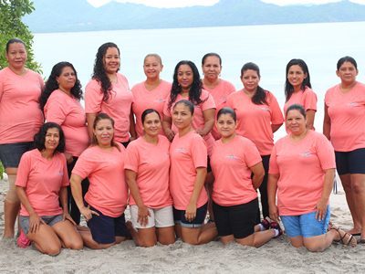 Meet the Team A photo of the entire housekeeping team of Special Places of Costa Rica. Two rows of smiling ladies, all wearing pink 'Special Places' t-shirts and posing on a beautiful tropical beach.